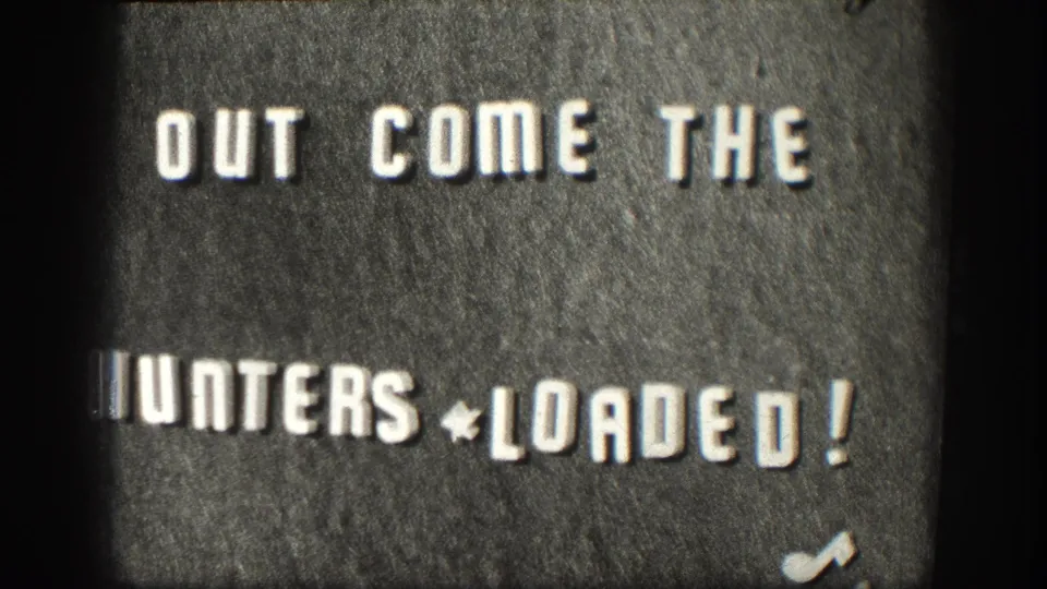 8mm title card circa 1958 reading 'OUT COME THE HUNTERS * LOADED!', held on screen with minor inter-frame exposure variation characteristic of 8mm reversal stock.