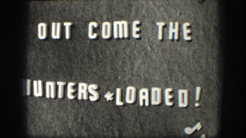Continued hold on 1950s 8mm title card: 'OUT COME THE HUNTERS * LOADED!' on dark textured board, Kansas hunting-trip reel, circa 1958.
