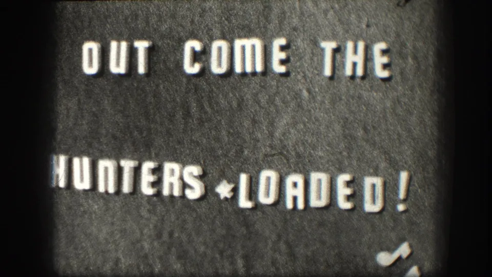 Home-movie intertitle on felt board, circa 1958 Kansas, reading 'OUT COME THE HUNTERS * LOADED!' — a DIY chapter-title card typical of mid-century amateur 8mm film.