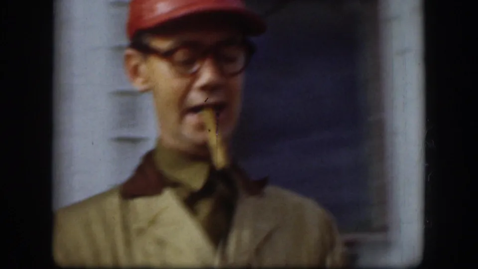 Close-up of man's face in slight profile, a possible cigarette or toothpick visible in his mouth, wearing a red work cap; Kansas, circa 1958, 8mm home movie.