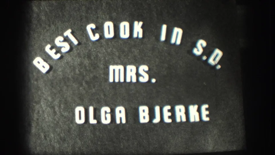 8mm home-movie title card circa 1958 identifying Mrs. Olga Bjerke as best cook in S.D., white stylized lettering on a dark field.