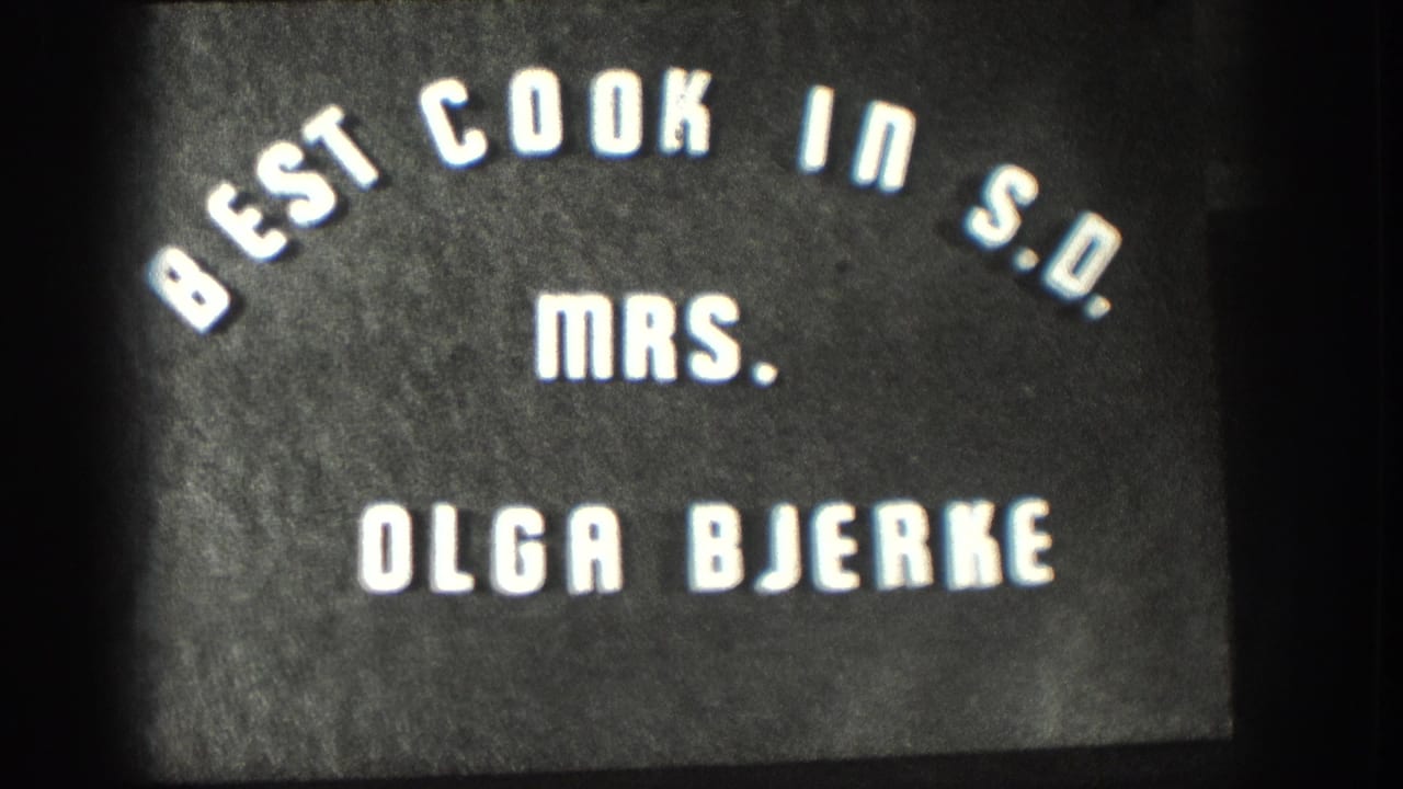 Repeated 8mm title-card frame circa 1958 holding on 'Best Cook in S.D. Mrs. Olga Bjerke' lettering on a dark field.