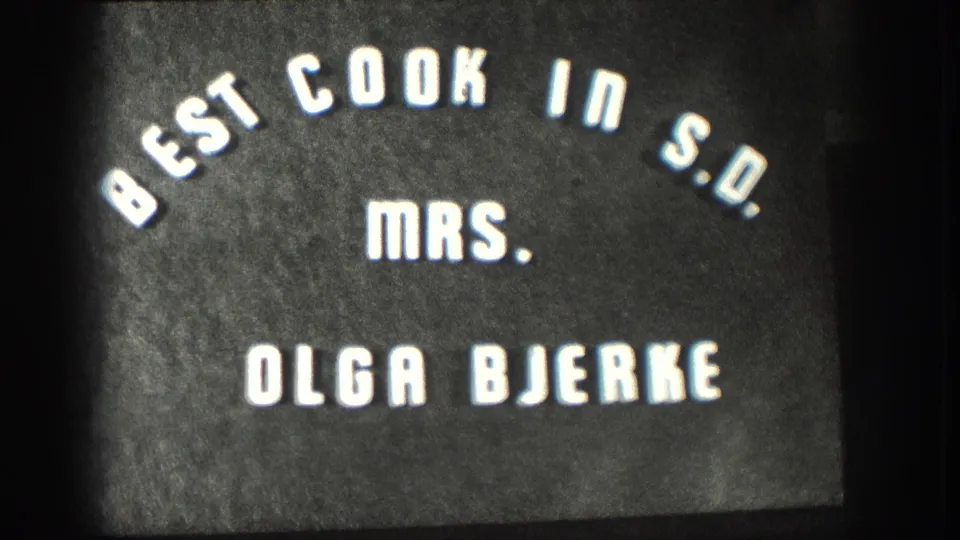 Repeated 8mm title-card frame circa 1958 holding on 'Best Cook in S.D. Mrs. Olga Bjerke' lettering on a dark field.