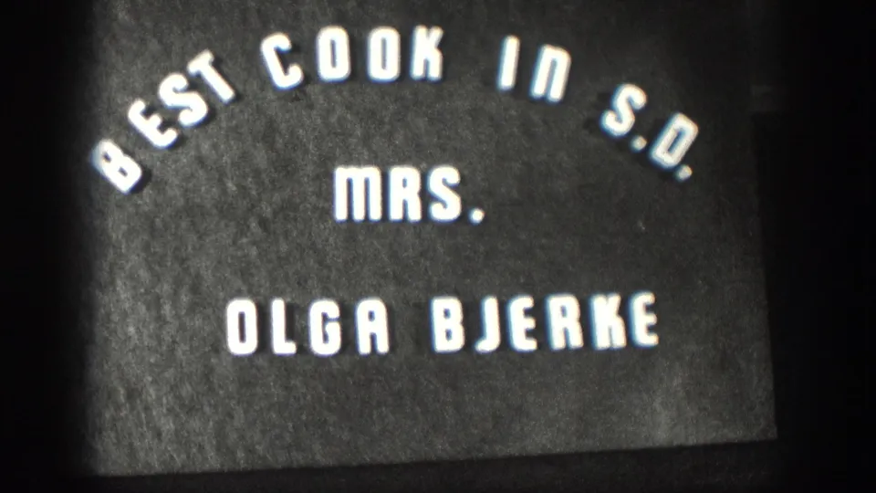 Third 8mm title-card frame circa 1958, still holding on the 'Best Cook in S.D. Mrs. Olga Bjerke' credit against a dark background.