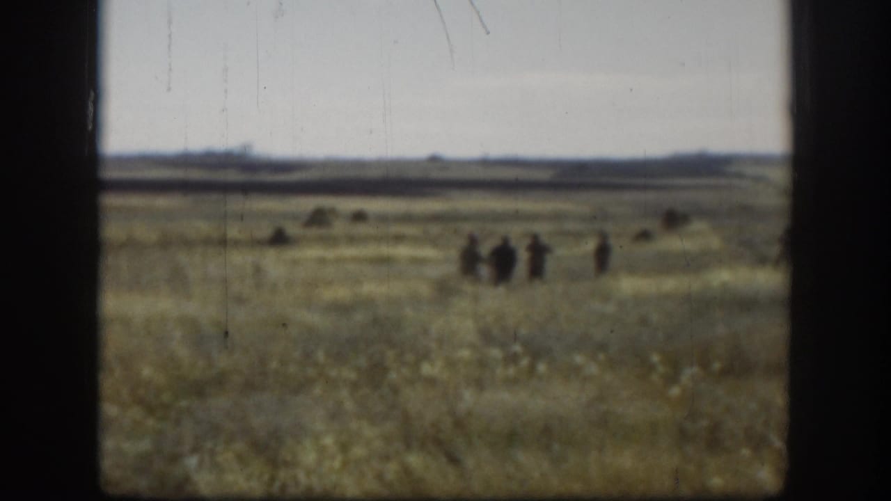 8mm home movie wide shot of a flat Kansas-area prairie, c.1958, with a small group of hunters walking in the mid-distance.