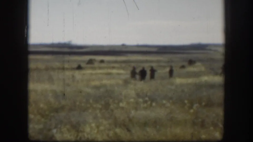 8mm home movie wide shot of a flat Kansas-area prairie, c.1958, with a small group of hunters walking in the mid-distance.