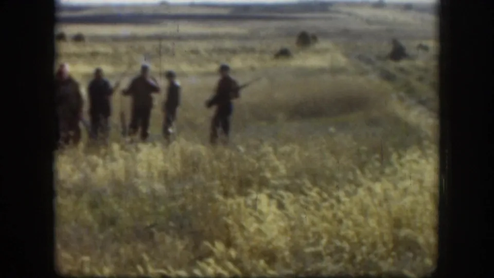 Mid-shot of approximately five men in casual outdoor jackets standing in tall dry grass, c.1958 Kansas, some carrying rifles or shotguns.