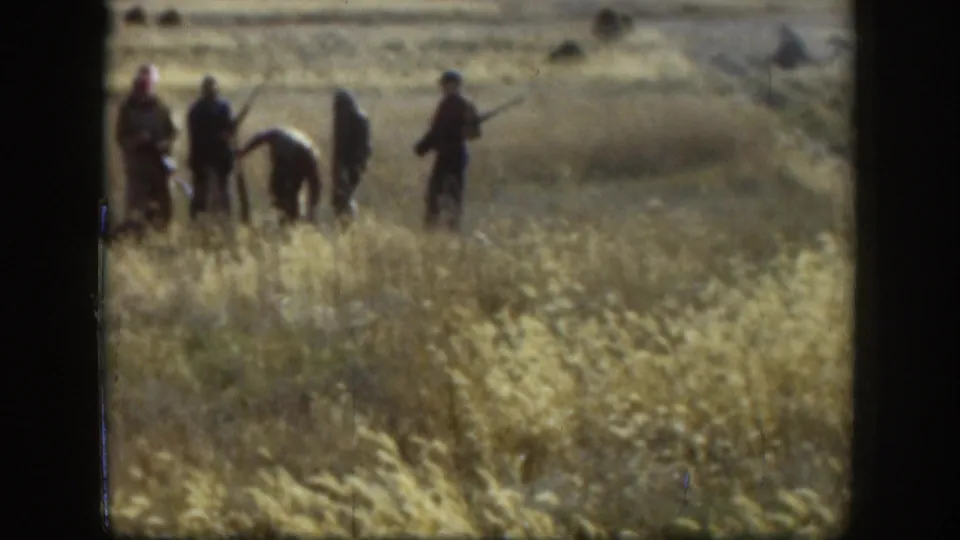 Group of hunters in dry Kansas grassland, c.1958; one man bends forward, possibly retrieving game, while companions hold firearms.