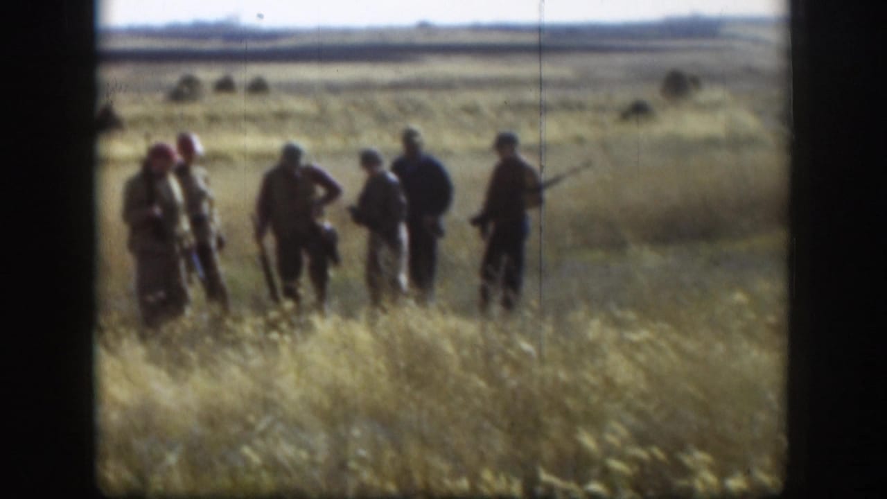 Wide shot of a hunting party of five or six men carrying shotguns in a dry Kansas prairie grass field, circa 1958, on 8mm color film.