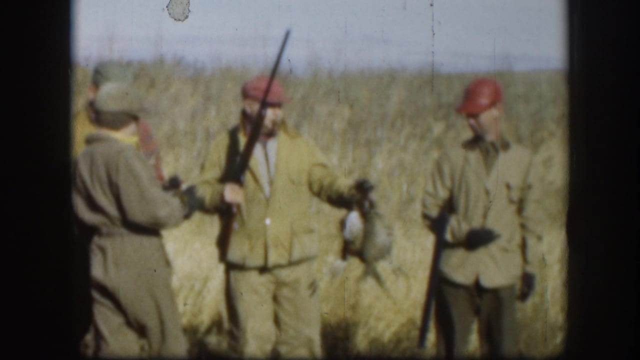 Three men in hunting attire standing in tall grass; one holds a shotgun while another appears to hold game birds.