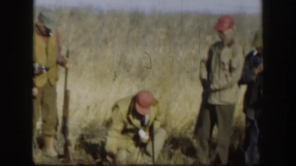Two men in late-1950s hunting attire, red caps and olive field jackets, in a golden Kansas prairie field during a pheasant hunt, circa 1958.