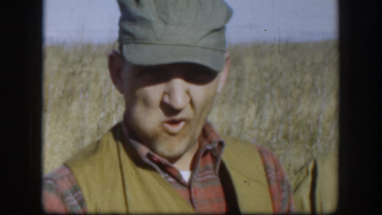 Hunter in plaid shirt, olive cap, and hunting vest photographed close-up in a flat Kansas wheat field, circa 1958.