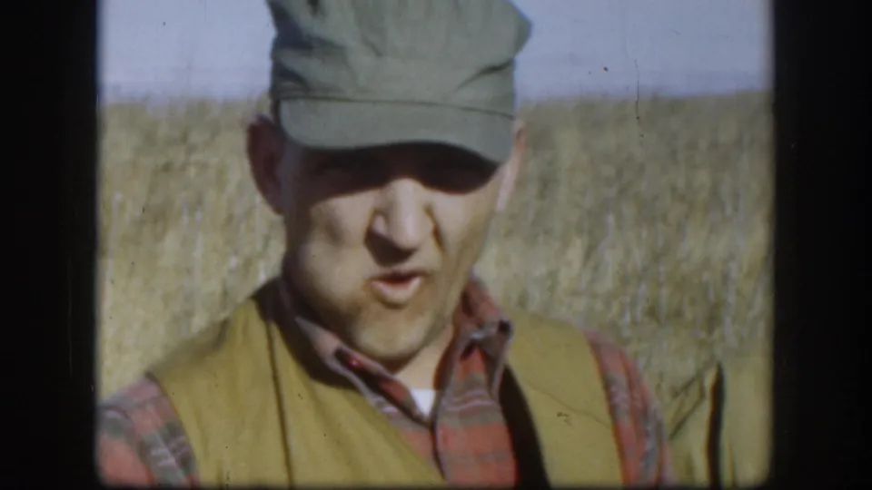 Hunter in plaid shirt, olive cap, and hunting vest photographed close-up in a flat Kansas wheat field, circa 1958.