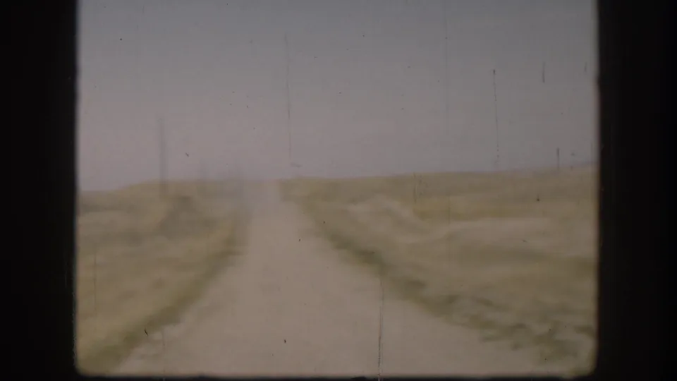 Straight gravel road receding to the flat Kansas horizon, open golden-brown fields on either side, circa 1958 8mm home movie footage.