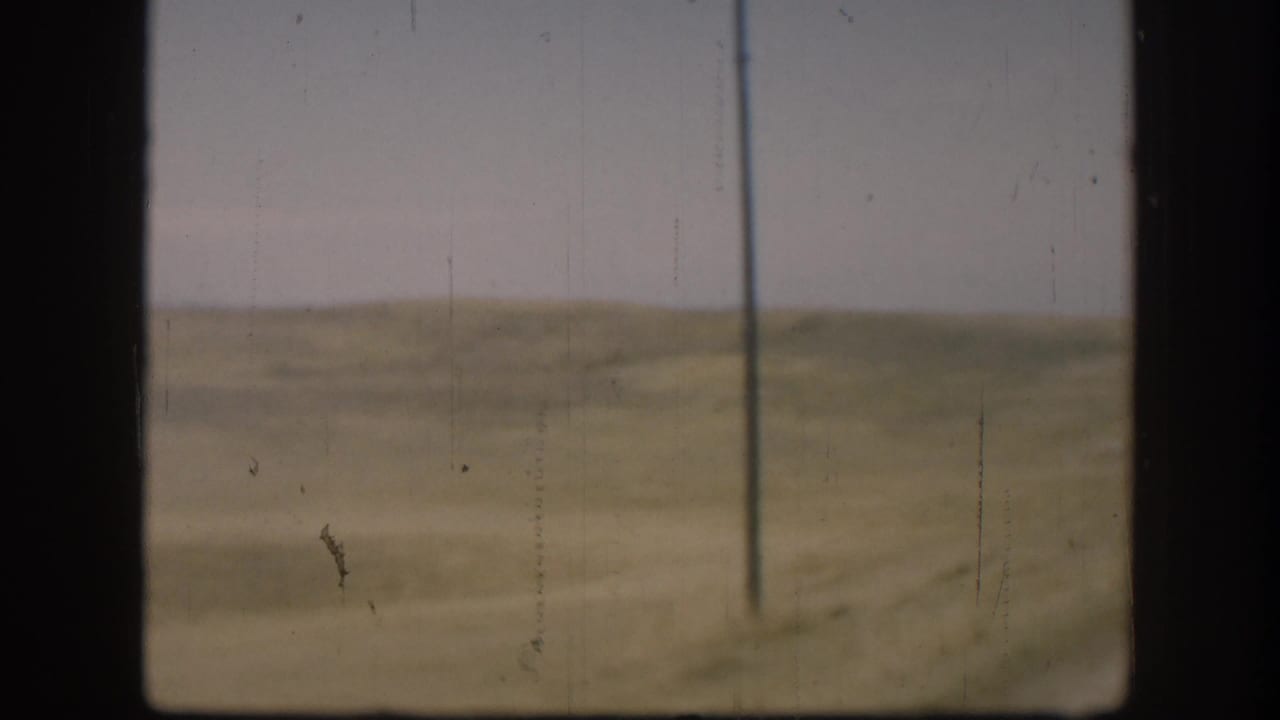 Open Kansas grassland with a single utility pole at right, shot from a moving vehicle, circa 1958 8mm home movie.