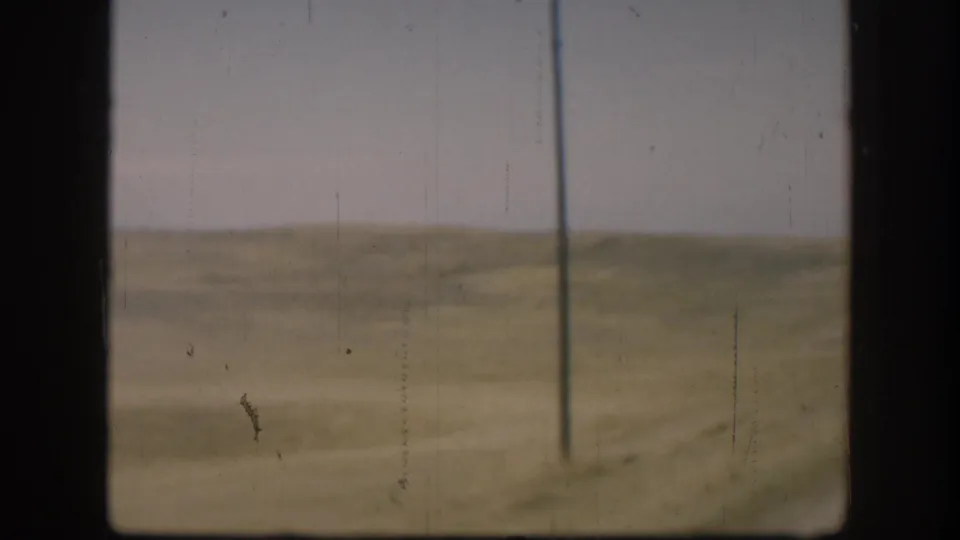 Open Kansas grassland with a single utility pole at right, shot from a moving vehicle, circa 1958 8mm home movie.