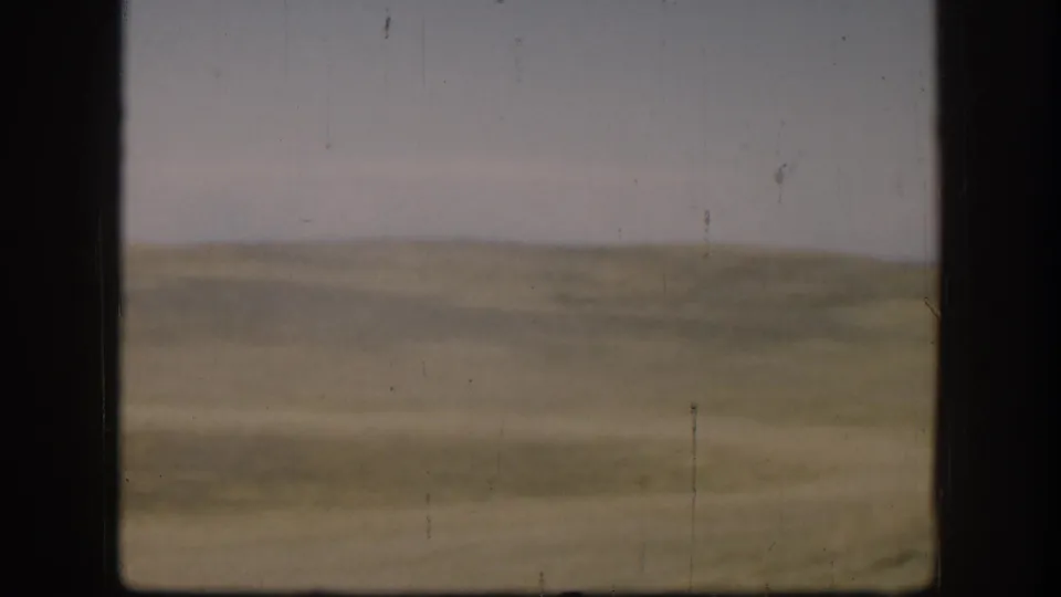 Wide empty Kansas plain under pale overcast sky, circa 1958, sparse composition with visible 8mm film scratches.
