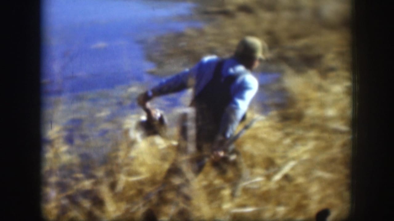 Man straightening up from a lakeside crouch while holding something low; 1950s 8mm home movie, possibly Kansas.