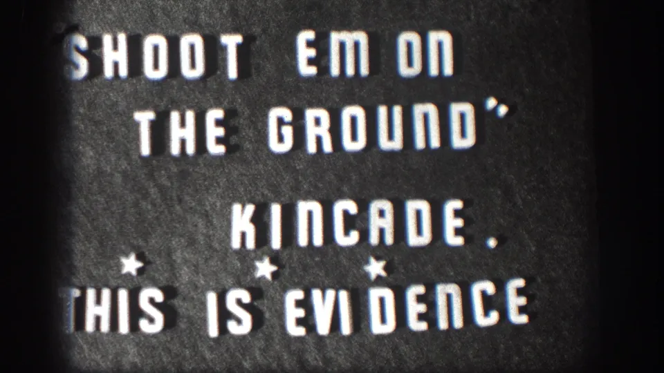 1958 Kansas 8mm home movie title card; white stencil letters on dark board read SHOOT EM ON THE GROUND, KINCADE, THIS IS EVIDENCE with star ornaments and edge vignette