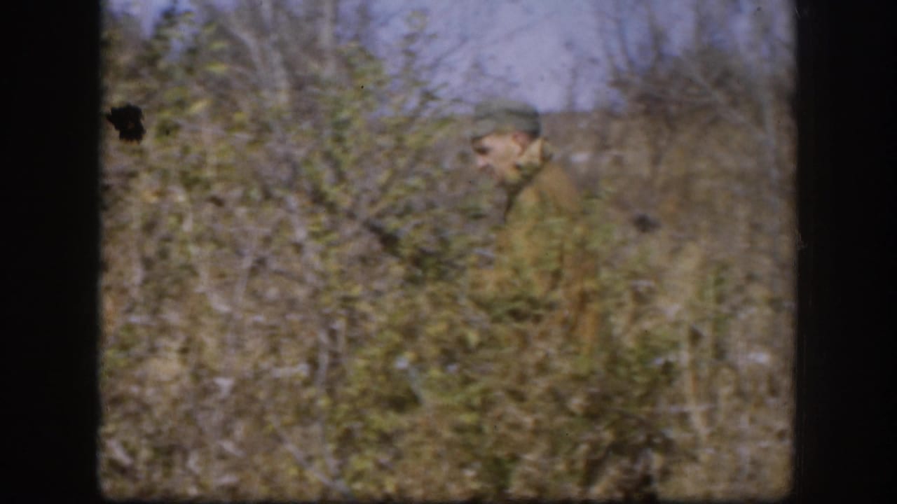 Hunter in camouflage-style jacket and pale cap moves through dense autumn brush, 8mm home movie, Kansas area circa 1958.