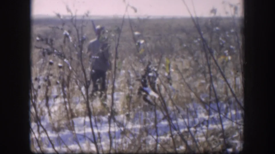 Two figures in the distance in a frost or lightly snow-covered open field with sparse dried stalks, 8mm home movie, Kansas area circa 1958.