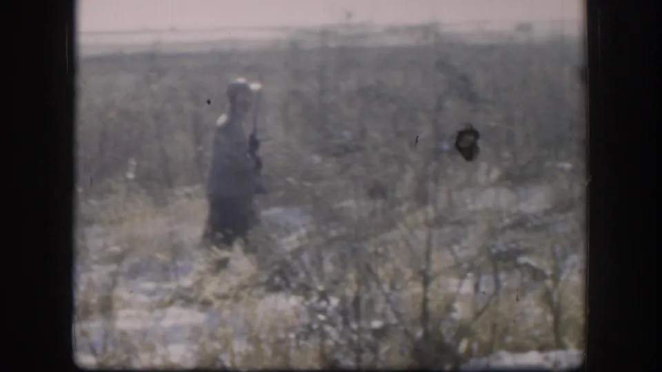1958 Kansas 8mm: hunter standing in an open snow-covered field under an overcast winter sky, flat Midwest landscape with dry grass stubble.