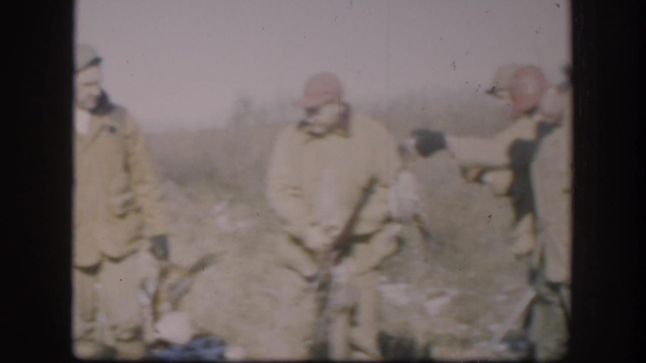 Three hunters in late-1950s attire with orange-red caps stand over harvested game in a flat, lightly snow-covered Kansas field, circa 1958.