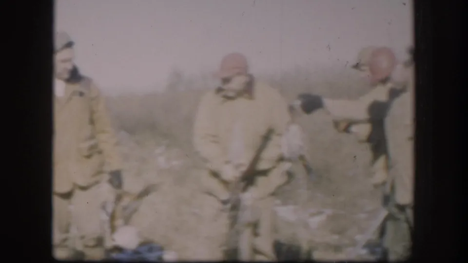 Three hunters in late-1950s attire with orange-red caps stand over harvested game in a flat, lightly snow-covered Kansas field, circa 1958.