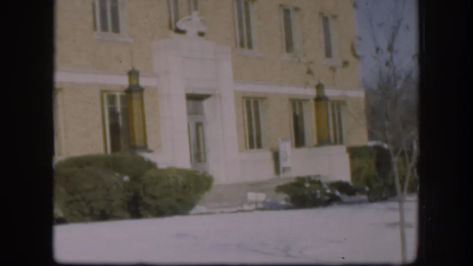 Continued wide shot of the beige brick courthouse front with classical stone trim and winter grounds, Kansas circa 1958, 8mm color film.