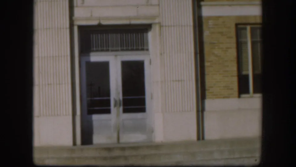 Clark County Courthouse main entrance, Kansas, 1958 — 8mm shot of double glass doors with decorative bar transom, fluted white columns, and concrete steps.