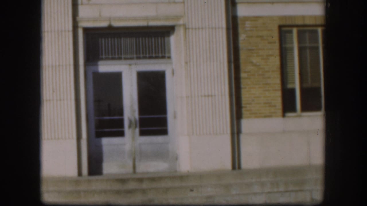 Exterior of what appears to be a civic or institutional building in Kansas, circa 1958 — fluted stone pilasters and glass doors, shot on 8mm film.