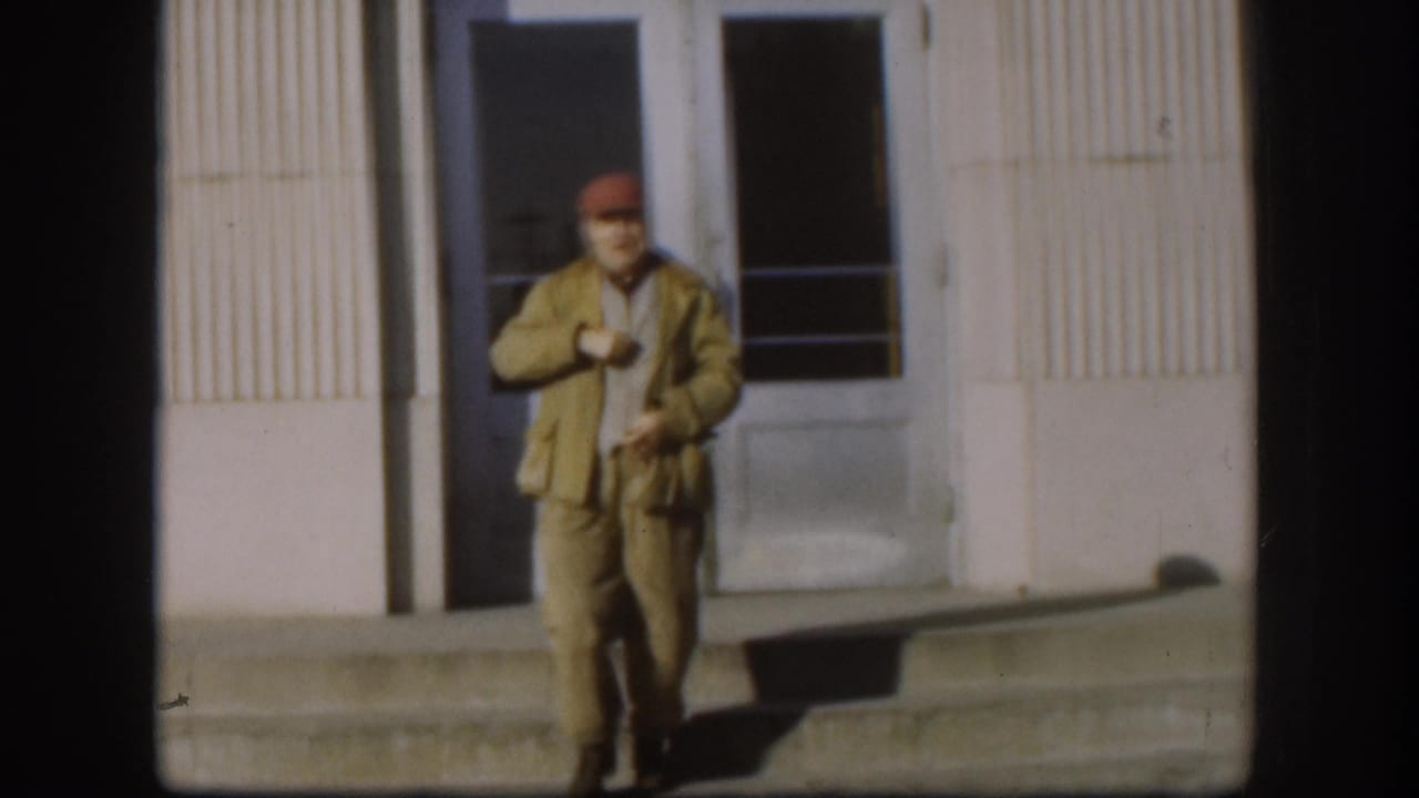 Man in red cap pauses on steps adjusting his jacket, vertical ribbed building facade and window visible behind him.