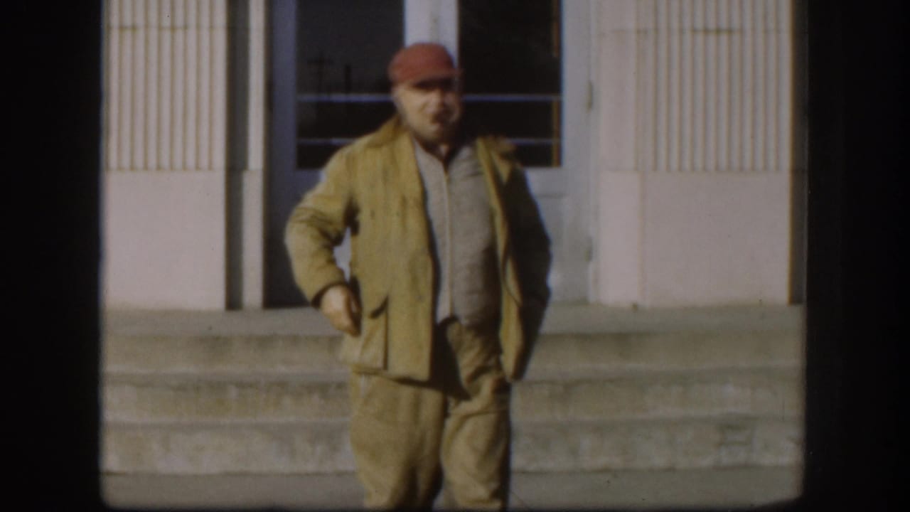 Full-body shot of a middle-aged man in a tan jacket and red cap on stone steps outside what appears to be a civic building, Kansas, circa 1958