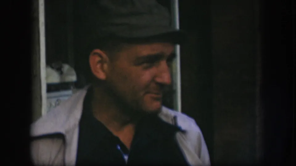 Man in grey cap and light jacket looks to the side in Kansas home movie circa 1958, an unposed candid moment.