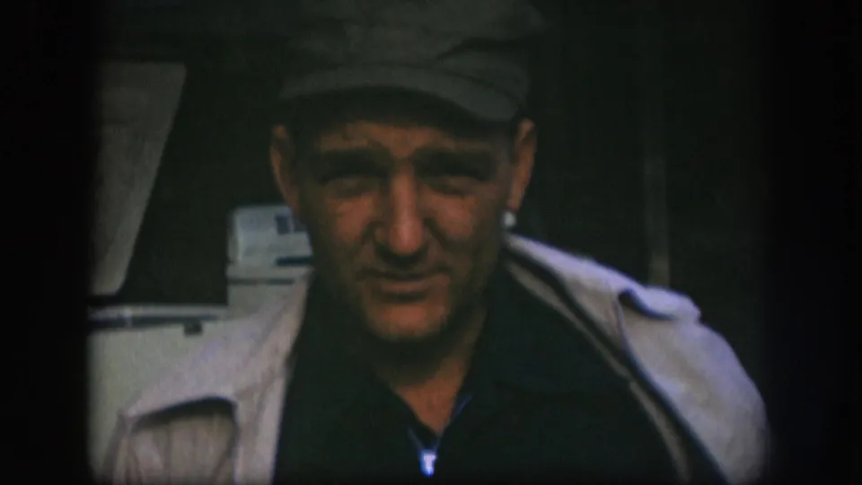 Man in dark flat cap looking directly into the camera with a relaxed expression; white appliance in background suggests a commercial storefront, consistent with Kansas 1958 metadata.