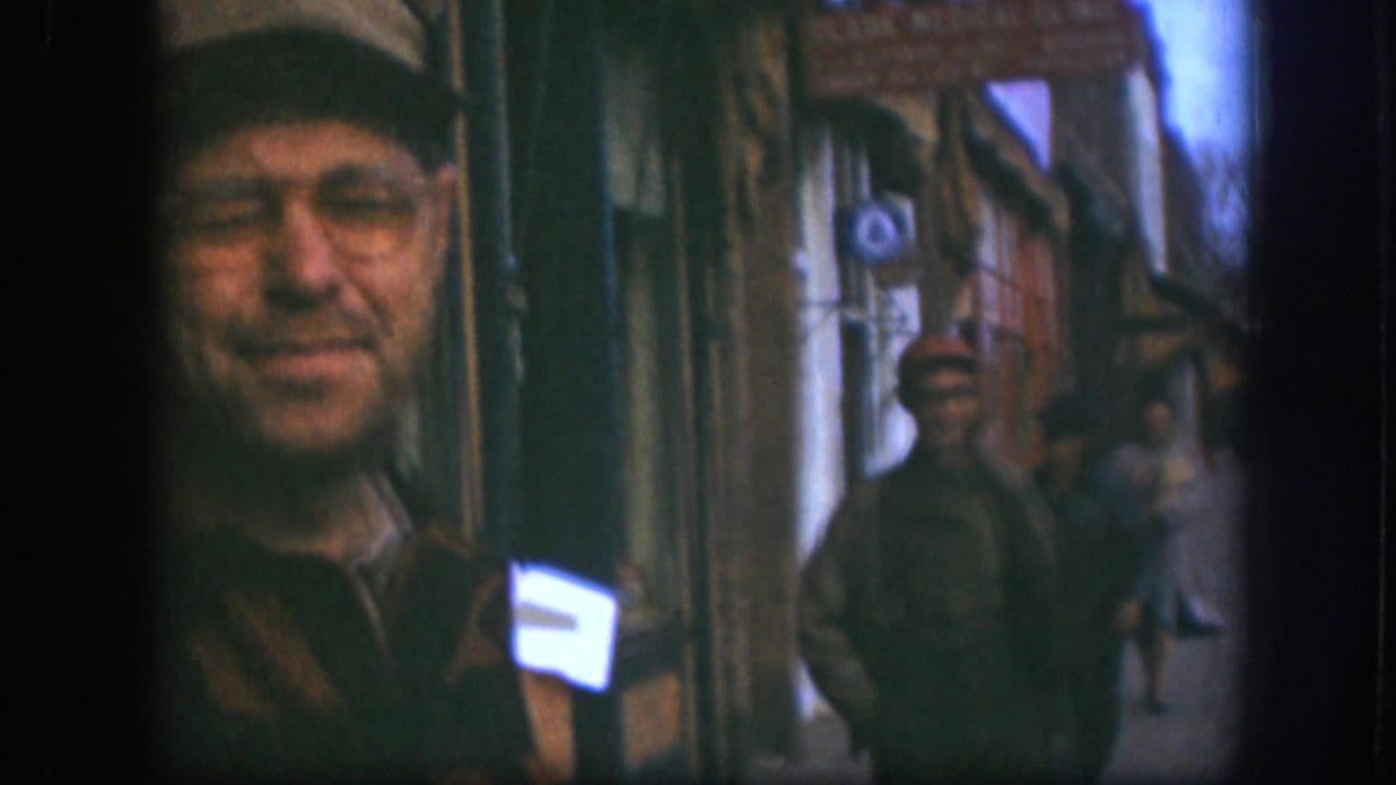 Candid close-up of a smiling man in a light cap and glasses on a Kansas commercial sidewalk, circa 1958, 8mm color home-movie footage.