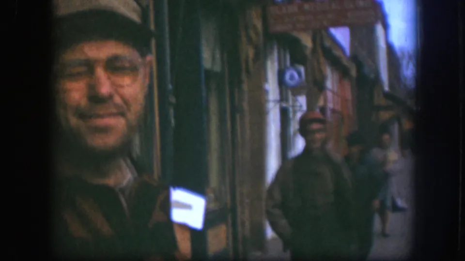 Candid close-up of a smiling man in a light cap and glasses on a Kansas commercial sidewalk, circa 1958, 8mm color home-movie footage.