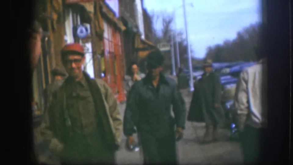 Two men near colorful storefronts on what appears to be a small Kansas main street, circa 1958; the man in the red cap faces the camera directly.