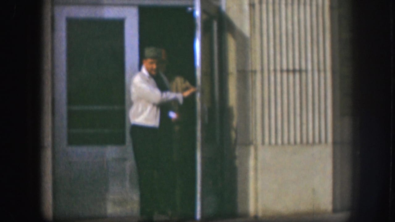 Two men at the entrance of a mid-century institutional building, Kansas, circa 1958; one in a light shirt holds or pushes open the glass door.