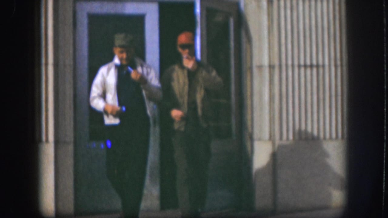 Two men in motion outside a ribbed-siding building identified as Kansas, 1958 per metadata; man in white shirt and tie appears to hold food or paper in both hands.