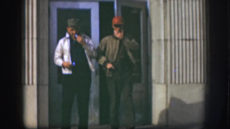 Closing frame of two men outside a ribbed-siding building identified as Kansas, 1958 per metadata; film-edge vignetting darkens the right margin of the frame.