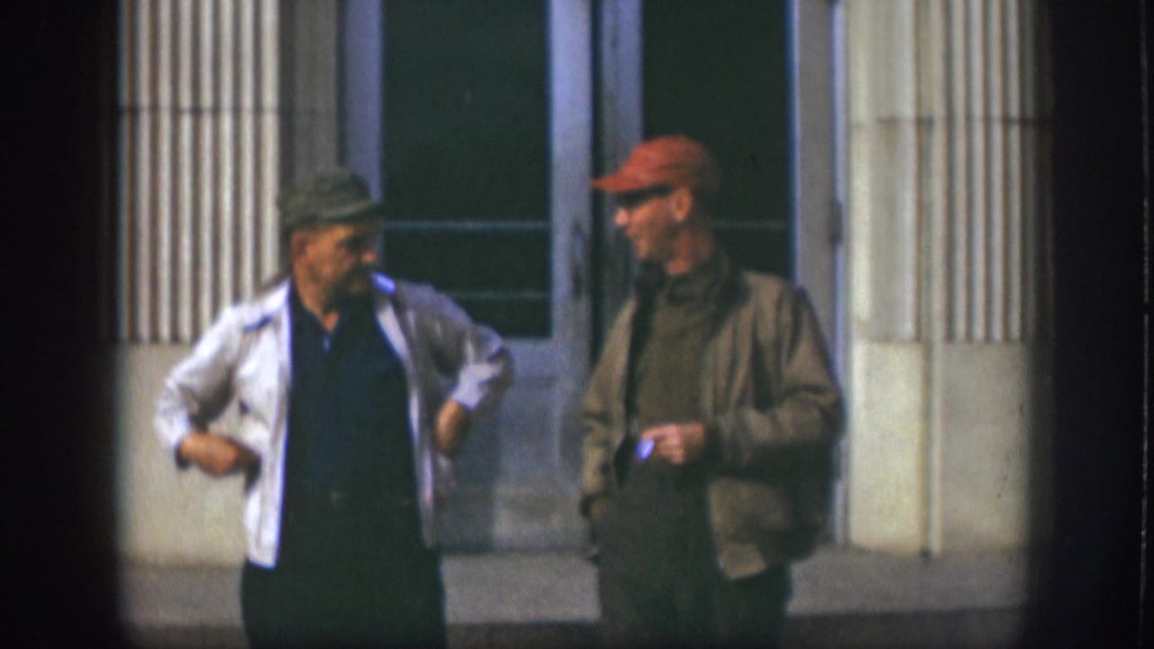 Two men near the end of a candid outdoor exchange outside a columned building in Kansas, USA, circa 1958; man in red cap appears to smile as companion gestures.
