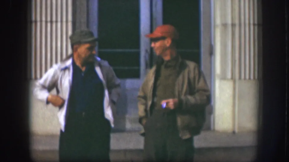 Two adult men in flat cap and red baseball cap conversing outside a columned building facade, Kansas USA, circa 1958.