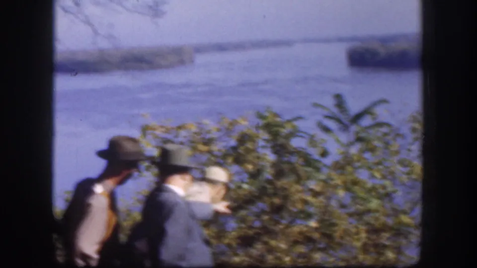 Two men wearing brimmed hats and jackets stand at an elevated overlook gazing toward a wide river with tree-covered islands, Kansas, USA, circa 1958.