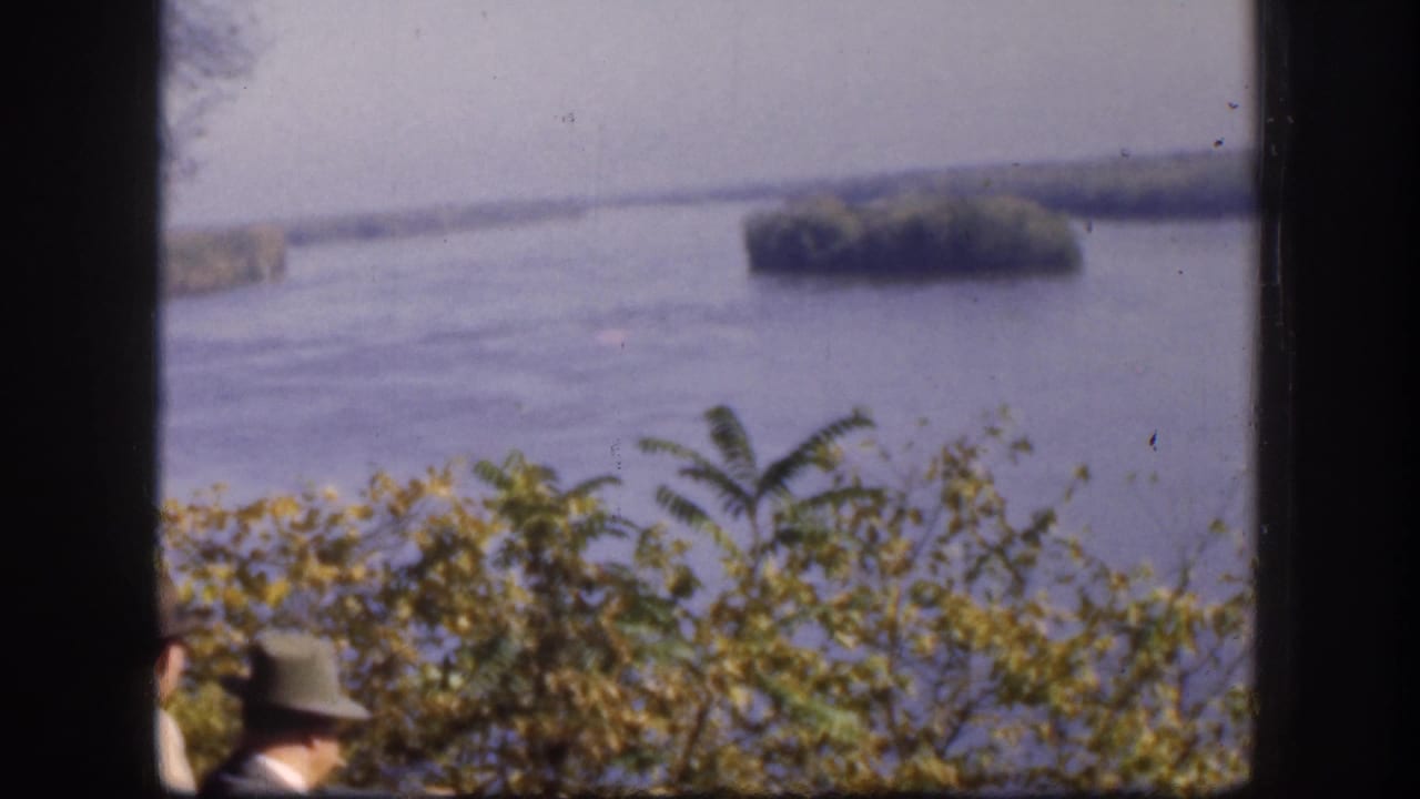 A man in a brimmed hat stands at the edge of a riverside overlook with a broad river dotted by tree-covered islands beyond, Kansas, USA, circa 1958.