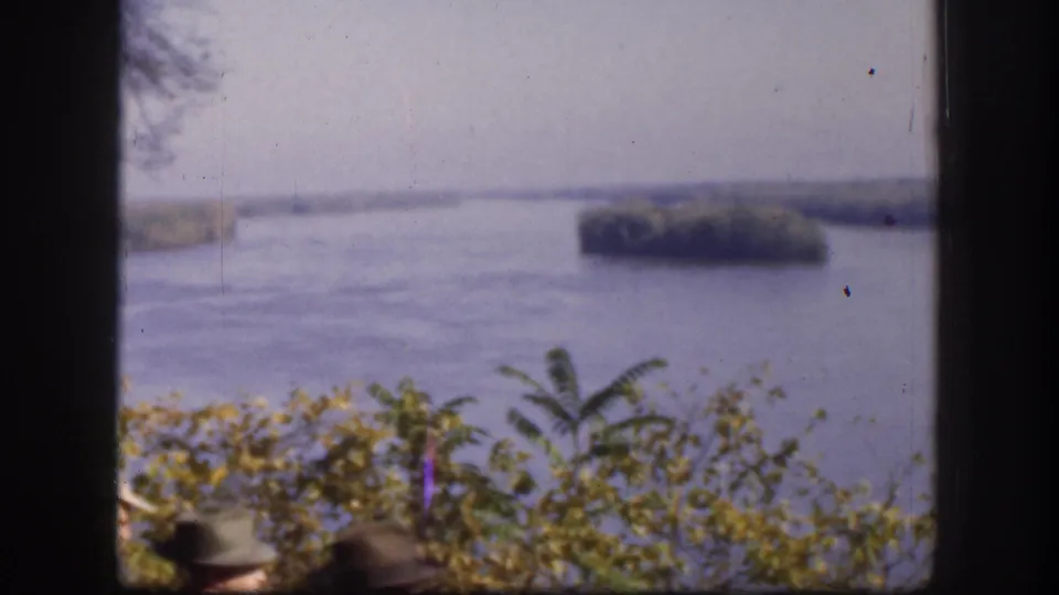 Broad river landscape with tree-covered islands shot from elevated overlook; a partial figure in a brimmed hat is just visible at the lower frame edge, Kansas, USA, circa 1958.