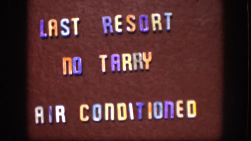 8mm home movie close-up of a roadside changeable letter board, Kansas, circa 1958; text reads LAST RESORT, NO TARRY, AIR CONDITIONED in blue, orange, and yellow plastic letters.