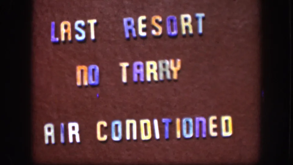 8mm home movie frame c. 1958 Kansas showing painted roadside sign with chromatic color distortion typical of aged reversal film stock.