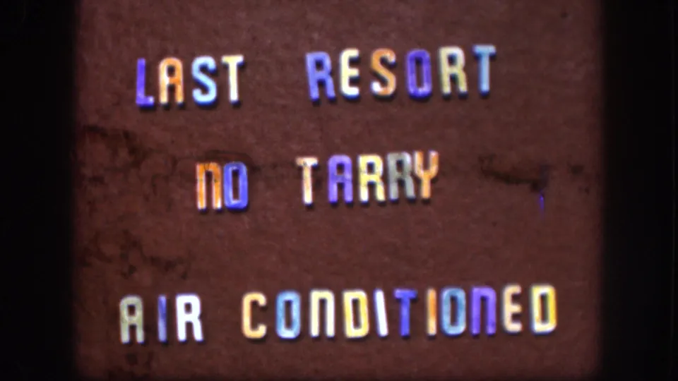 8mm film frame c. 1958 Kansas showing roadside lodging sign; grain, scratches, and dust spots visible in lower frame, consistent with original 8mm stock aging.