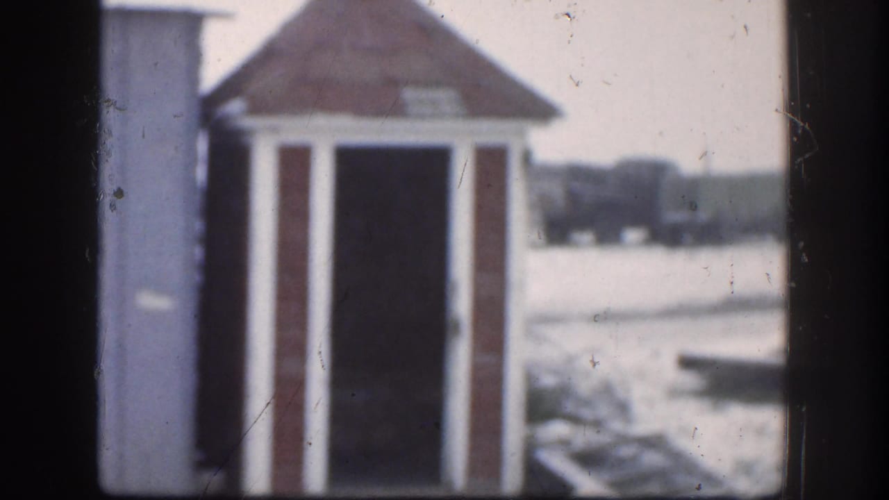 1958 Kansas home movie frame showing a small wooden outhouse with a red-shingled roof against a snowy rural landscape.